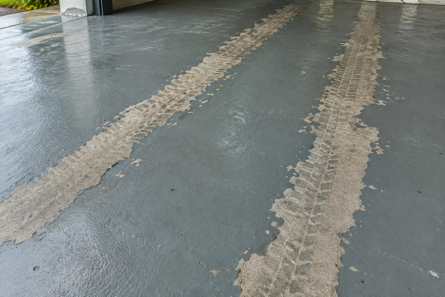 Two strips of grey floor paint worn away in the tyre tracks, showing tread marks on bare concrete